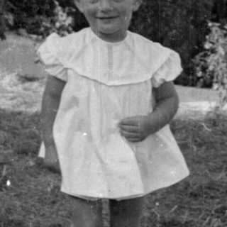 Young child in a white dress standing outdoors.