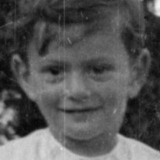 Young child in a white dress standing outdoors.
