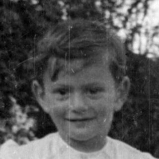 Young child in a white dress standing outdoors.
