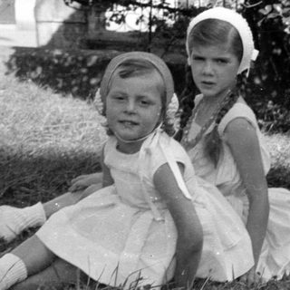 Two girls in white dresses sitting on grass.