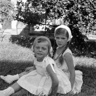 Two girls in white dresses sitting on grass.