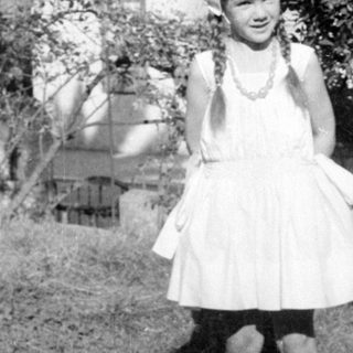 Girl in white dress standing before a house.