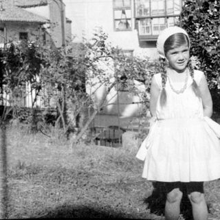 Girl in white dress standing before a house.