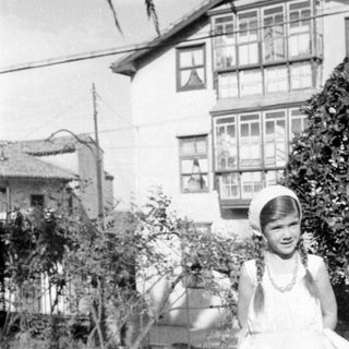 Girl in white dress standing before a house.