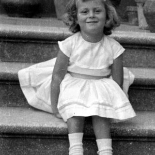 Young girl in white dress sitting on stone stairs.