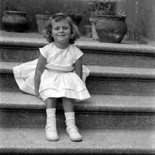 Young girl in white dress sitting on stone stairs.