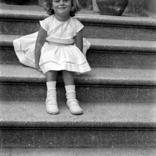 Young girl in white dress sitting on stone stairs.