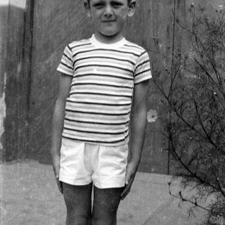 Boy in striped shirt and shorts by wooden door.