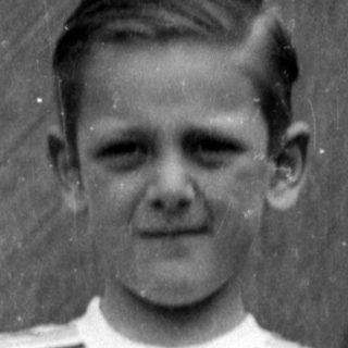 Boy in striped shirt and shorts by wooden door.