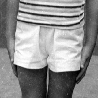 Boy in striped shirt and shorts by wooden door.