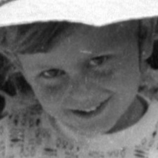 Child in sun hat holding a doll outdoors.