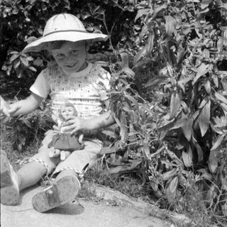 Child in sun hat holding a doll outdoors.