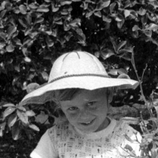 Child in sun hat holding a doll outdoors.