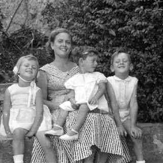 Woman and three children sitting outdoors by foliage.