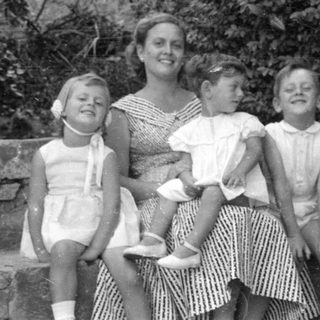 Woman and three children sitting outdoors by foliage.
