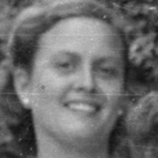 Woman and three children sitting outdoors by foliage.