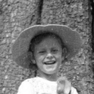 Child in hat holding animal by a large tree.