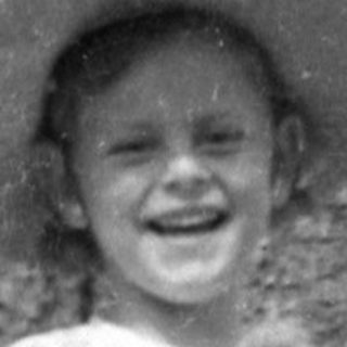 Child in hat holding animal by a large tree.