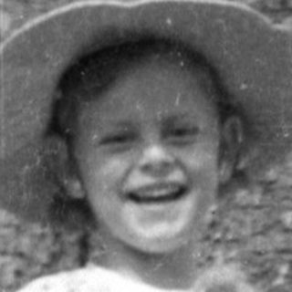 Child in hat holding animal by a large tree.