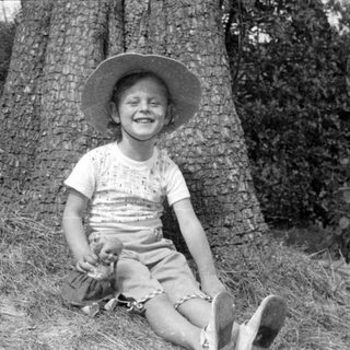 Child in sun hat sitting by a tree.