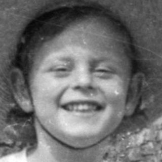 Child in sun hat sitting by a tree.
