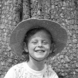 Child in sun hat sitting by a tree.