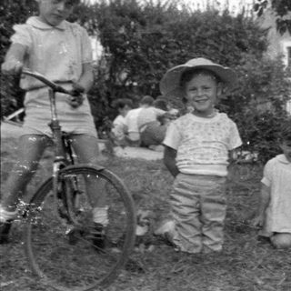 Three children with a bicycle in a yard.
