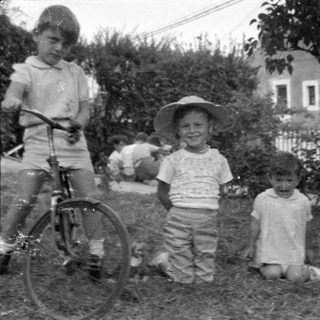 Three children with a bicycle in a yard.