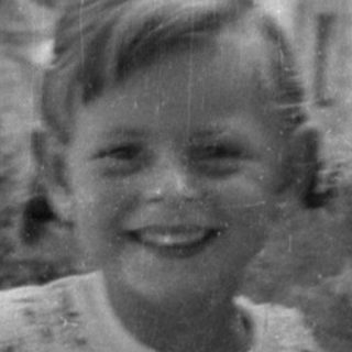 Smiling child holding a doll outdoors.
