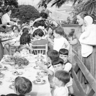 Outdoor meal with adults and children under palm tree.