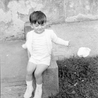 Young child in white clothing sitting on concrete.