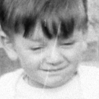 Young child in white clothing sitting on concrete.