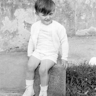 Young boy in cardigan sitting on stone block.