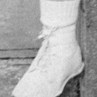 Young boy in cardigan sitting on stone block.