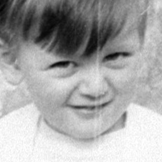 Young boy in cardigan sitting on stone block.