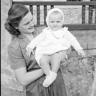 Woman holding a baby in a white bonnet.