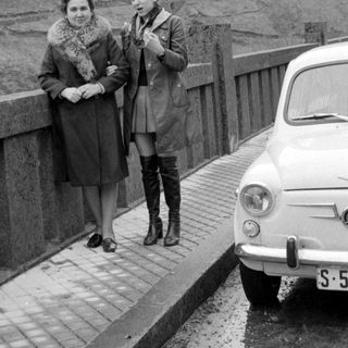 Two women standing on a bridge beside a car.