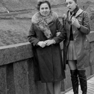 Two women standing on a bridge beside a car.