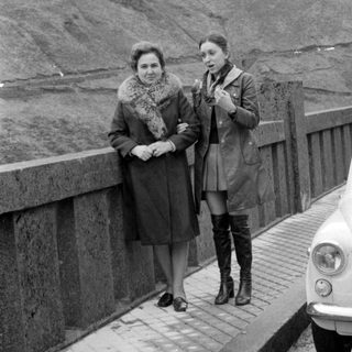 Two women standing on a bridge beside a car.