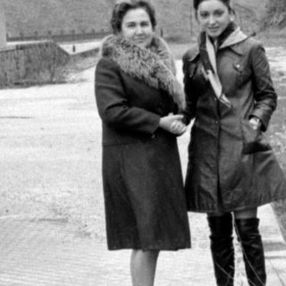 Two women standing on a platform by a mountain.