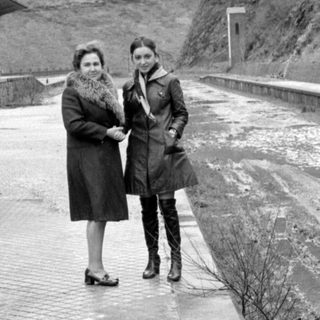 Two women standing on a platform by a mountain.