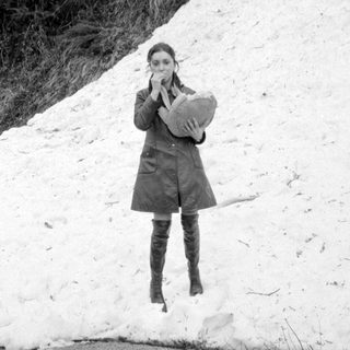 Woman in coat and boots by snow pile.