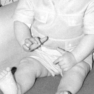 Infant lying on patterned fabric next to furniture.