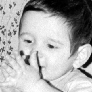 Infant in light-colored outfit lying on patterned fabric.