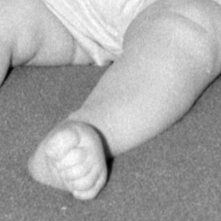 Infant in light-colored outfit lying on patterned fabric.