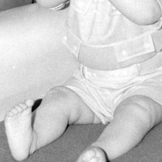 Infant in light-colored outfit lying on patterned fabric.