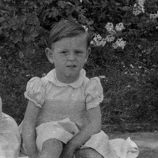 Two children in ruffled dresses sitting outdoors.
