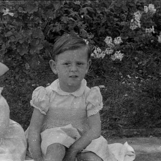 Two children in ruffled dresses sitting outdoors.