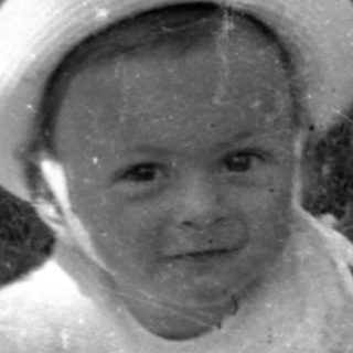 Young child in a hat sitting outdoors.