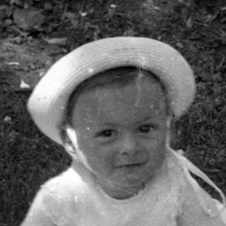 Young child in a hat sitting outdoors.